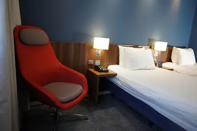 a red chair sitting next to a bed in a hotel room at Holiday Inn Express Harlow by IHG in Harlow