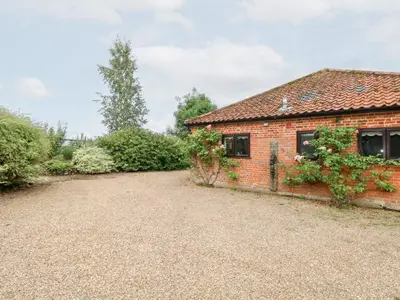 a brick house with a gravel driveway in front of it at Lowbrook Cottage in Diss