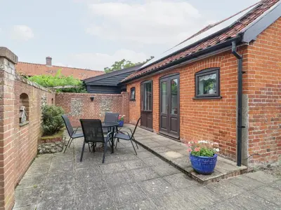 a patio with a table and chairs and a building at Lowbrook Cottage in Diss