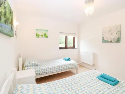 a bedroom with two beds and a chandelier at Lowbrook Cottage in Diss