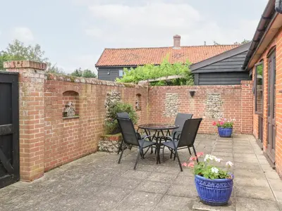 a patio with a table and chairs and a brick wall at Lowbrook Cottage in Diss