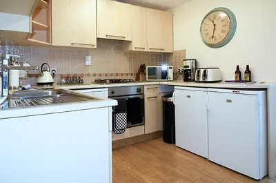 a kitchen with white cabinets and a clock on the wall at Sunshine Corner in West Mersea