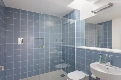 a blue tiled bathroom with a toilet and a sink at The Fieldbarns at Bullocks Farm in Bishops Stortford