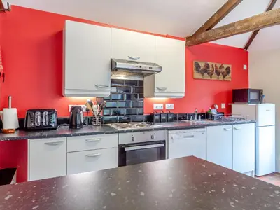a kitchen with white cabinets and red walls at The Nest Box in Diss