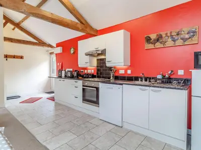 a kitchen with white cabinets and a red wall at The Hen House in Diss
