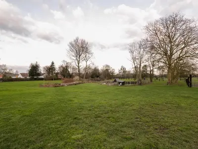 a large green field with trees and a barn at The Granary in Halstead