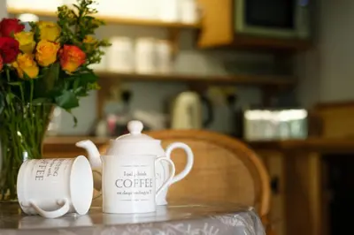 a table with a coffee pot and a vase of flowers at Quavers Rest - quintessential little home & hot tub available ! in Rushford