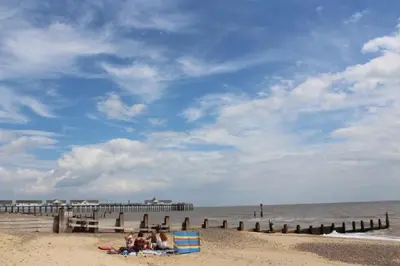 a group of people sitting on the beach near a pier at Corner Farm Barn in Halesworth