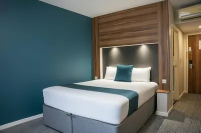 a large bed in a room with a blue wall at Ramada London Stansted Airport in Stansted Mountfitchet