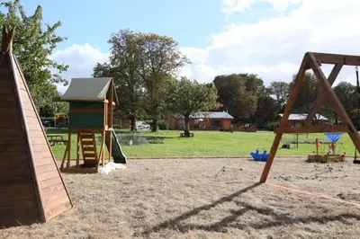 a playground with a wooden swing set and a building at The Orchard Bramble Lodge in Hadleigh