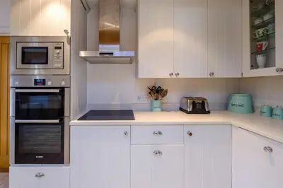 a kitchen with white cabinets and silver appliances at Meare House in Thorpeness