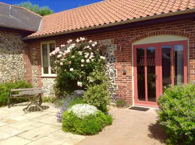 a brick house with a bench and a bush with flowers at Lackford Lakes Barns in Flempton