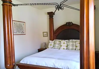a bedroom with a wooden canopy bed with white sheets at Lackford Lakes Barns in Flempton