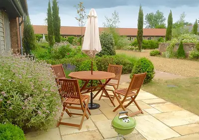 a table and chairs with an umbrella on a patio at Lackford Lakes Barns in Flempton