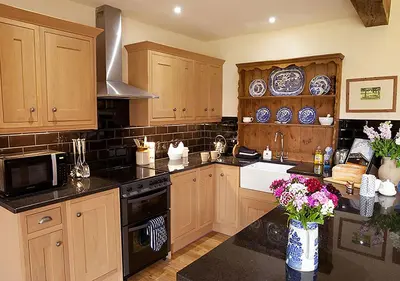 a kitchen with wooden cabinets and black counter tops at Lackford Lakes Barns in Flempton