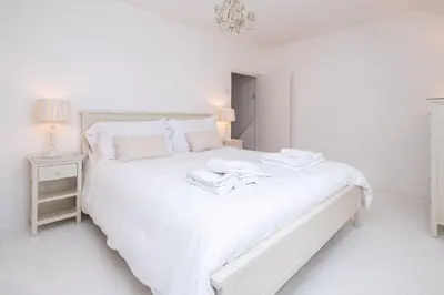 a white bedroom with a white bed with two towels on it at Puddleduck Cottage in Aldeburgh