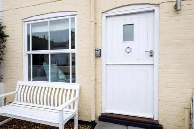 a white door and a bench in front of a house at Puddleduck Cottage in Aldeburgh
