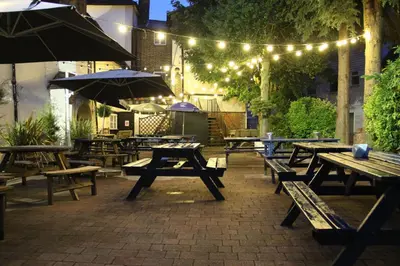 an outdoor patio with wooden tables and umbrellas and lights at The Blue Boar - Maldon in Maldon
