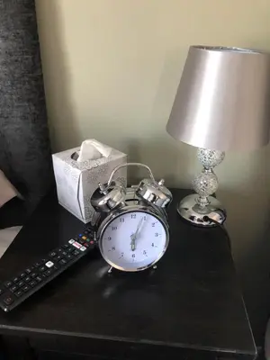 a alarm clock sitting on a table with a lamp and a remote control at By Buildersbeds - Hill House 3 Bedrooms in Romford