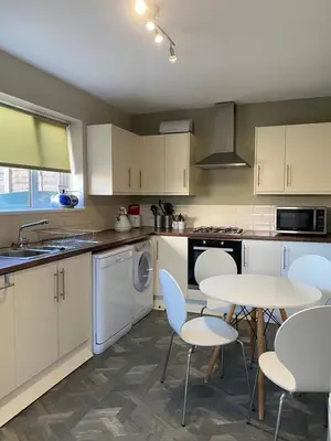 a kitchen with white cabinets and a table and chairs at By Buildersbeds - Hill House 3 Bedrooms in Romford