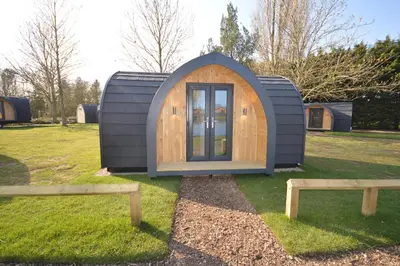 a tiny house in a field with two benches at Camping Pods, Carlton Meres Holiday Park in Rendham