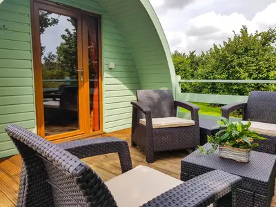 a patio with chairs and tables on a green house at Colemans Cottage Fishery in Wickham Bishops