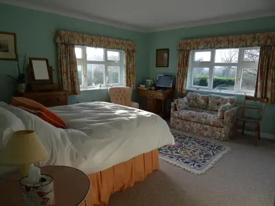 a bedroom with a bed and a chair and windows at The Newnham White House in Baldock