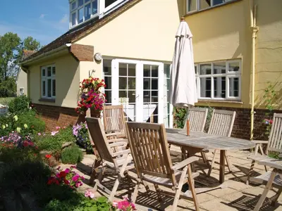 a patio with a wooden table and chairs and an umbrella at The Newnham White House in Baldock
