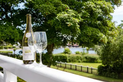 a bottle of wine and two wine glasses on a fence at Lake Cottage - A large holiday home in Thorpeness - Close to the beach and The Meare - Aldeburgh Coastal Cottages in Thorpeness