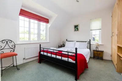 a bedroom with a bed and a chair and windows at Lake Cottage - A large holiday home in Thorpeness - Close to the beach and The Meare - Aldeburgh Coastal Cottages in Thorpeness