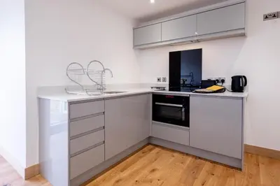 a kitchen with white cabinets and a wooden floor at Oak - Three Tuns Apartments, Pettistree, Wickham Market - by Aldeburgh Coastal Cottages in Pettistree