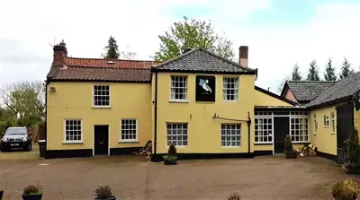 a yellow house with dogs sitting outside of it at The Pelican Guesthouse in Ashwellthorpe