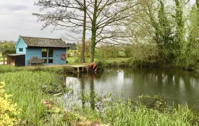a blue house sitting next to a river at Partridge Lodge Self Catering houses in Woodbridge