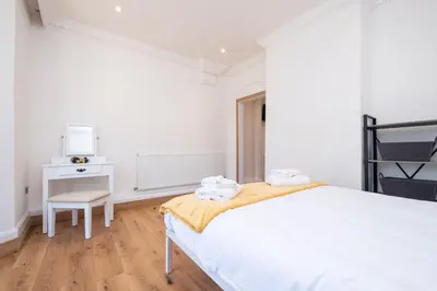 a white bedroom with a bed and a chair at Birch - Three Tuns Apartments - Pettistree, Wickham Market - by Aldeburgh Coastal Cottages in Pettistree