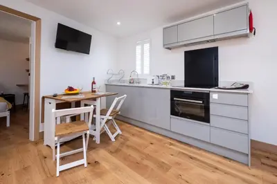 a kitchen with white cabinets and a table with chairs at Weeping Willow - Three Tuns Apartments, Pettistree, Wickham Market - by Aldeburgh Coastal Cottages in Pettistree