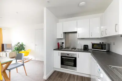 a kitchen with white cabinets and a table and chairs at Hertford Serviced Apartments in Hertford