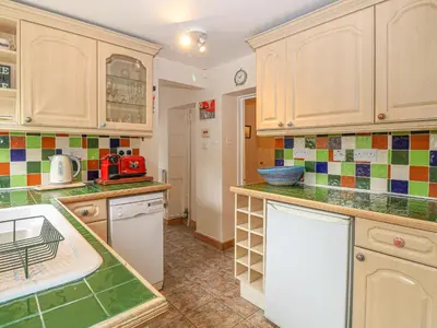 a kitchen with wooden cabinets and green tiles on the wall at 3 Station Cottages in Wymondham