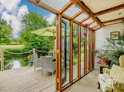 a conservatory with a deck with a table and chairs at 16th Century Cartlodge with private hot tub in Diss