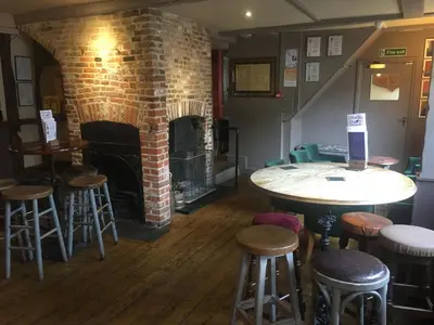 a room with a brick fireplace and tables and stools at Black Buoy Inn in Wivenhoe