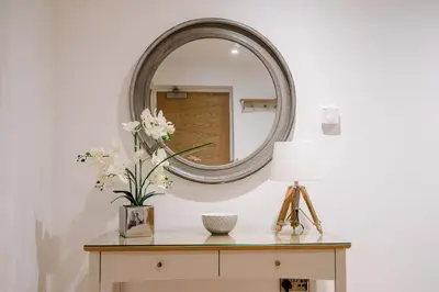 a mirror on a wall next to a table with flowers at 8 Deben Wharf, Woodbridge in Woodbridge