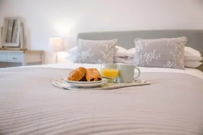 a breakfast tray with bread and orange juice on a bed at 8 Deben Wharf, Woodbridge in Woodbridge