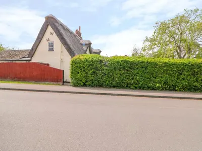 a house with a thatched roof and a red fence at Beaumont's Cottage in Cambridge