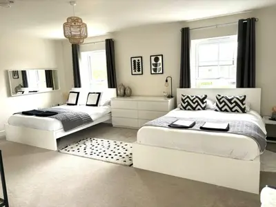two beds in a white bedroom with a mirror at Stansted Coach House - Apartment Hotel in Elsenham