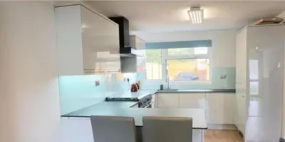 a white kitchen with a counter and chairs in it at Corporate Large Modern 4 to 5 Bedroom House in Bishops Stortford