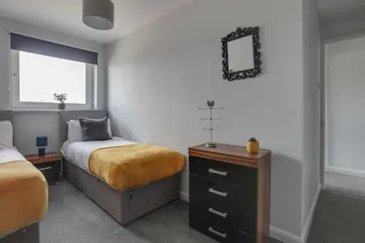a bedroom with two beds and a dresser and a mirror at Niche Sunrise Townhouse in Chelmsford
