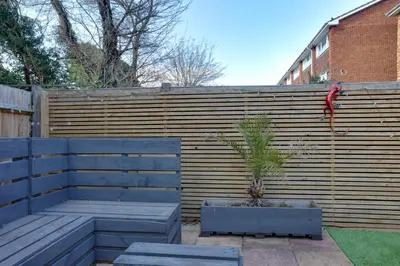 a wooden fence with a bench and a plant at Niche Sunrise Townhouse in Chelmsford