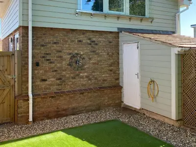 a brick building with a white door and green grass at Rainbows End in Saint Lawrence