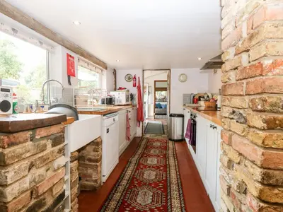 a kitchen with white cabinets and a brick wall at Garden House in Thetford