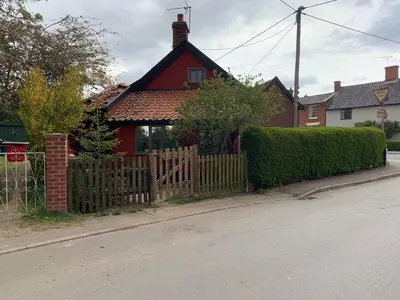 a red house with a wooden fence next to a street at Myrtle cottage in Dickleburgh