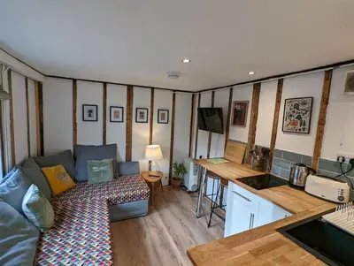 a living room with a couch and a table and a kitchen at Cobweb Cottage Studios in Spooner Row